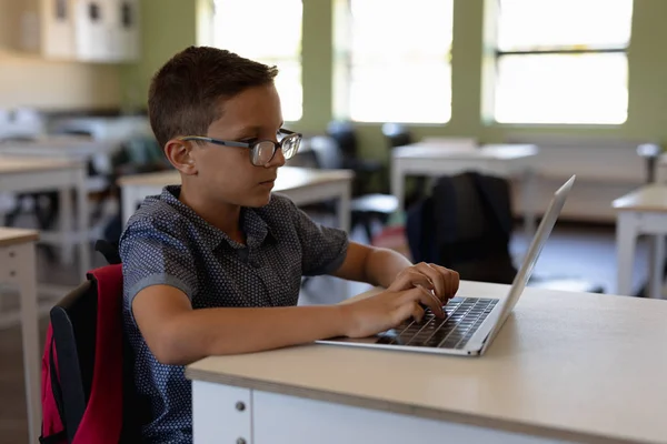 在小学教室里 一个戴着眼镜的白人学童坐在书桌旁 用笔记本电脑 侧视近景 — 图库照片
