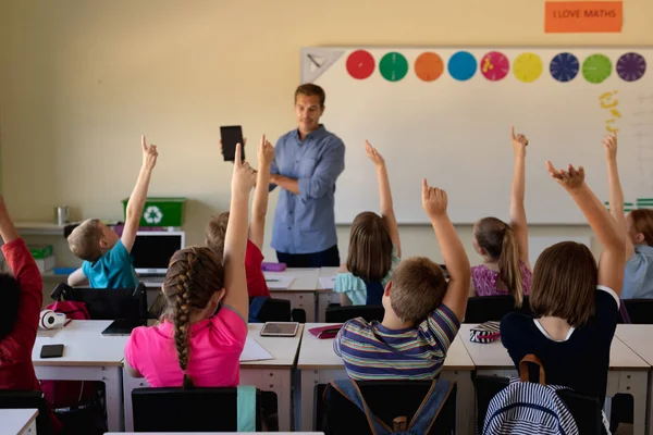 一个白人男教师站在教室前 拿着平板电脑 对着一群各种各样的学童讲话 — 图库照片