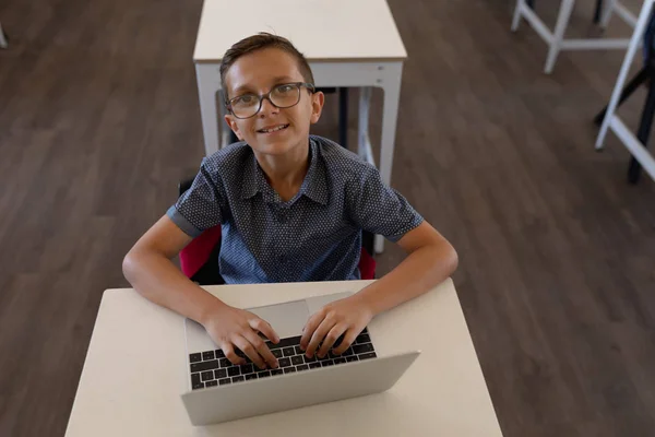 在小学教室里 一个戴着眼镜的白人学童坐在书桌前 用笔记本电脑 面带微笑地仰视着相机 高视阔别 — 图库照片