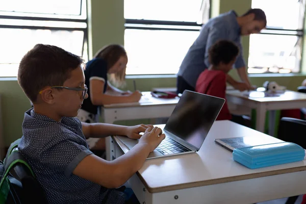 在小学课堂上 一个戴着眼镜的白人学童坐在课桌旁使用笔记本电脑的侧视图 — 图库照片