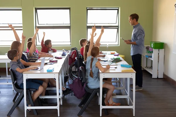 一个白人男教师站在教室前 手持平板电脑 对着一群各种各样的学童讲话的侧视图 — 图库照片