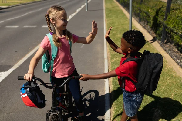 舗装された道路には赤いTシャツを着たアフリカ系アメリカ人の少年が自転車を持っていて 晴れた日には小学校に行く途中でハイタッチしています — ストック写真