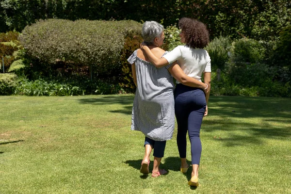 一个年长的混血种族妇女和她的成年女儿在花园里散步 拥抱和交谈的后视镜 — 图库照片