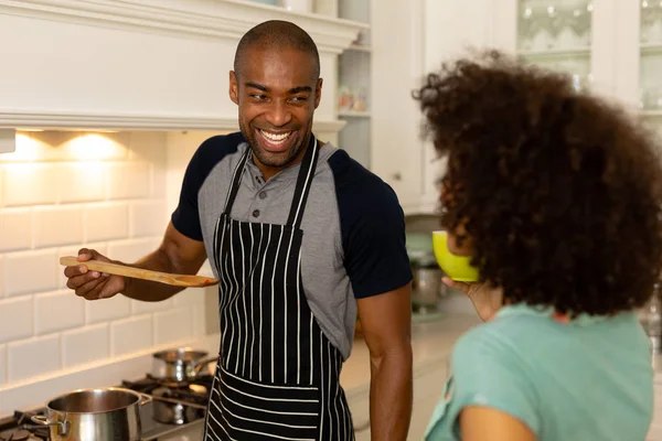 一对混血儿站在厨房里 男人面带微笑 用木勺给女人提供食物 — 图库照片