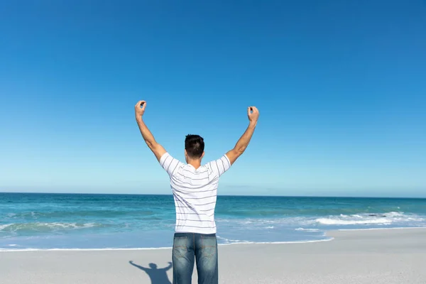一个白种人站在海滩上 背后是蓝天和大海 举起胳膊的侧视图 — 图库照片