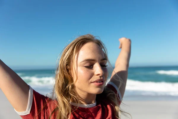青い空と海を背景にビーチに立って目を閉じて彼女の腕を上げる — ストック写真