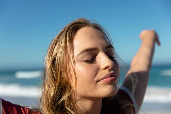 青い空と海を背景にビーチに立って目を閉じて彼女の腕を上げる — ストック写真