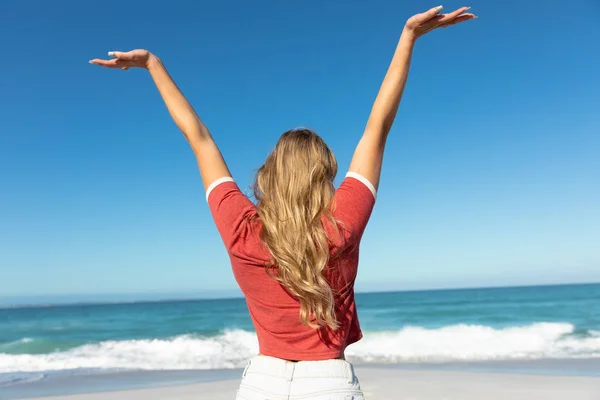 一个白种人女人的后视镜 她留着一头长长的金发 背对着蓝天和大海站在海滩上 张开双臂 — 图库照片