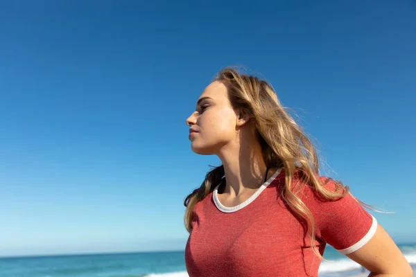 長いブロンドの髪をした白人女性のサイドビュー 背景に青い空と海とビーチに立って 離れて見て — ストック写真