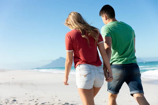 青い空と海を背景に 砂浜を歩き手を取りながら海岸沿いの白人夫婦の後ろの景色 — ストック写真