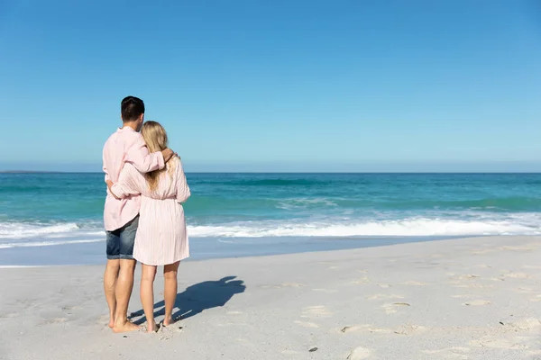青い空と海に囲まれたビーチに立つ白人のカップルの後ろの景色 抱擁と離れて見て — ストック写真