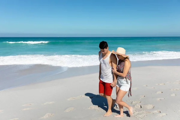 青い空と海を背景に 手を取りながらビーチを歩く白人カップルの側面図 — ストック写真