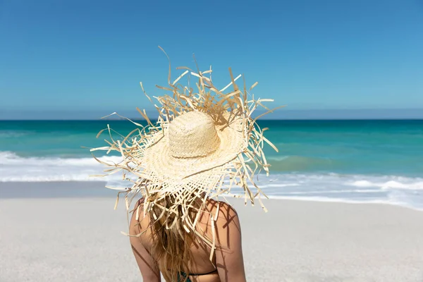青い空と海を背景にビーチに立って遠くを見ると わらの帽子をかぶった白人女性の後ろの景色 — ストック写真