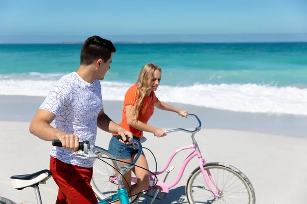 一对白种人夫妇骑着自行车在沙滩上散步的侧视图 背景是蓝天和大海 — 图库照片