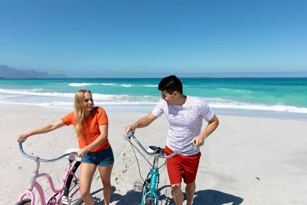 一对白种人夫妇在沙滩上散步 背景是蓝天蓝海 微笑着驾驶着他们的自行车 — 图库照片