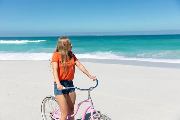 一个白种人站在沙滩上 背景是蓝蓝的天空和大海 骑着自行车 望向远方 — 图库照片