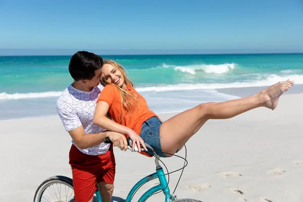 旁边是一对白种人夫妇在沙滩上散步的画面 背景是蓝天和大海 他们骑着自行车 玩得很开心 — 图库照片