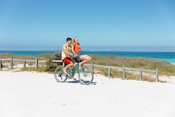 背景为蓝天蓝海的一对白种人夫妇骑自行车玩乐的侧视图 — 图库照片