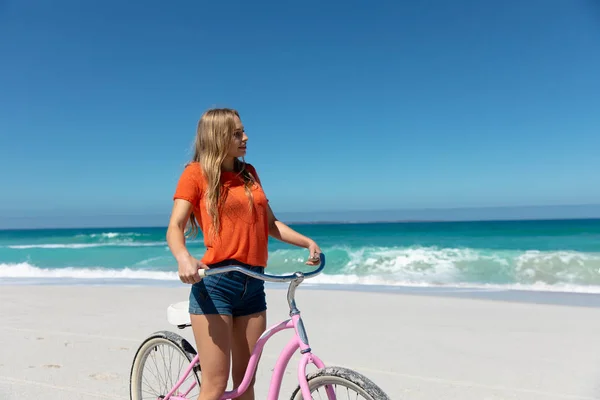 青い空と海を背景にビーチを歩く白人女性のサイドビュー 自転車をリードし 離れて見て — ストック写真