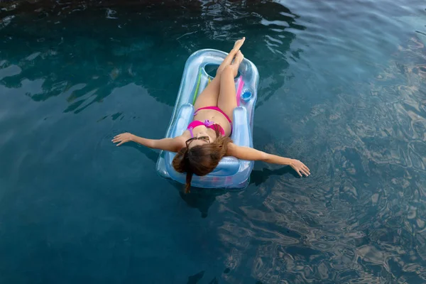 在阳光明媚的日子里 一个身穿泳衣和太阳镜的白人妇女躺在一个充气水池上 躺在游泳池里晒太阳 双手浸在水里的后视镜 — 图库照片