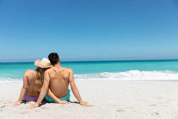 青い空と海を背景にビーチに横たわっている白人のカップルの背面ビュー 抱擁と離れて見て — ストック写真