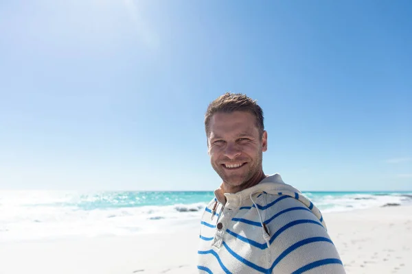 一个白种人站在海滩上 背对着蓝天和大海 微笑着对着镜头的前景 — 图库照片