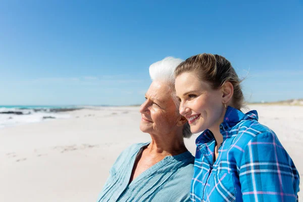 一个白种人妇女和她的母亲站在沙滩上 背景是蓝天蓝海 拥抱着 望着远方的侧影 — 图库照片