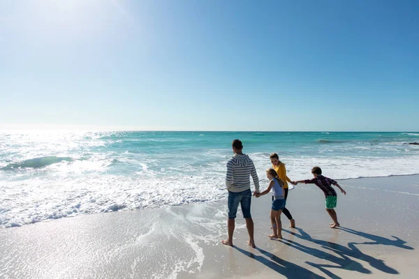 青い空と海を背景にしたビーチでの白人家族の背面ビュー 水の中を歩くと手を握って — ストック写真