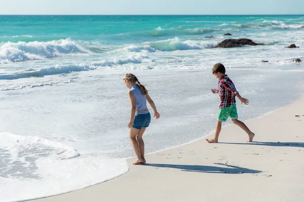 背景是蓝天蓝海的沙滩上的白人兄弟姐妹的侧视图 他们走向水面 玩得很开心 — 图库照片