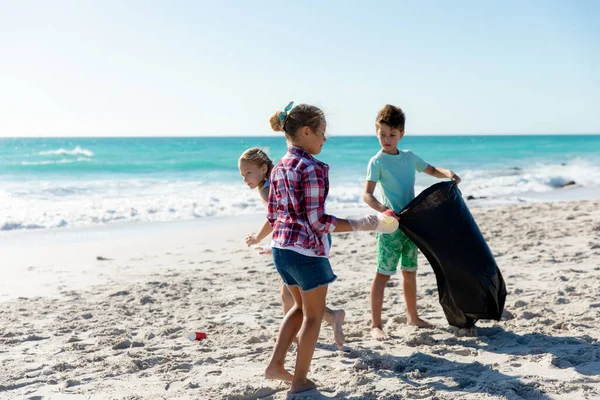 背景为蓝天蓝海的海滩上的白人兄弟姐妹们的前景 捡起垃圾 放进垃圾袋 — 图库照片