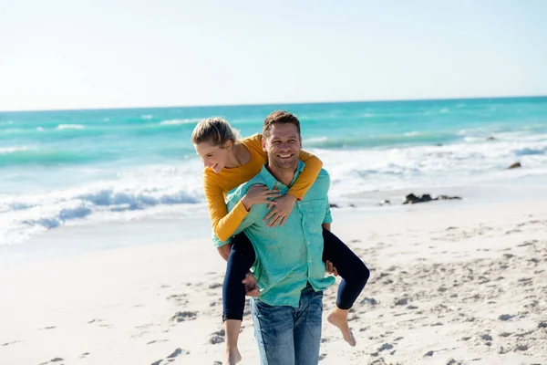 青い空と海を背景にビーチに立つ白人夫婦のフロントビュー ピギーバックと笑顔 — ストック写真