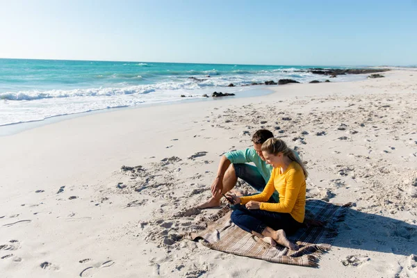 背景には青い空と海が広がるビーチに横たわっている白人のカップルの側面図 彼らのスマートフォンを受け入れ見て — ストック写真