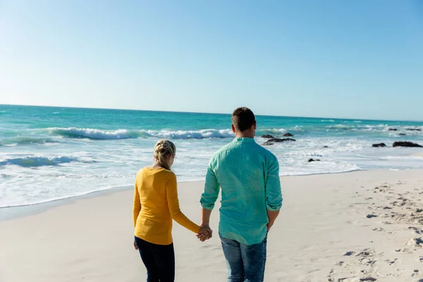 青い空と海を背景に 手を取りながらビーチを歩く白人夫婦の後ろの景色 — ストック写真