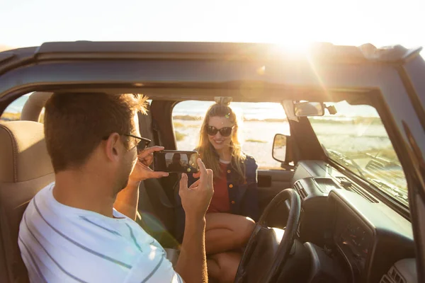 彼女の写真を撮る オープントップの車の中で笑みを浮かべて彼のガールフレンドと白人男性の側の高い角度ビュー — ストック写真