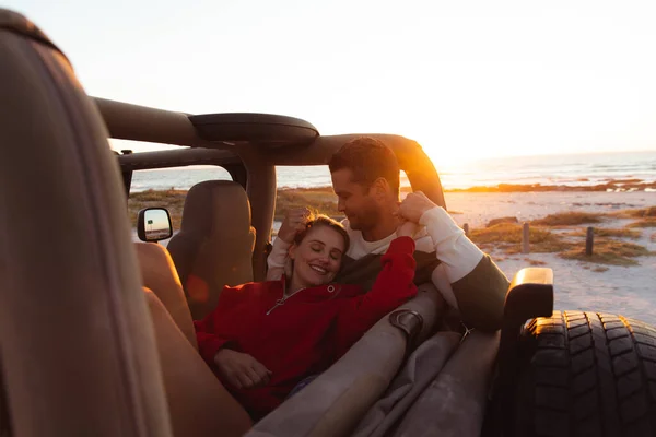 一对白种人夫妇坐在敞着的顶层轿车里 背景是夕阳西下的海滩 牵着手 玩得很开心 — 图库照片