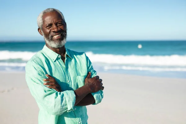 一个非洲裔美国老人的画像 他站在海滩上 背景是蓝天和大海 微笑着交叉着双臂拍照 — 图库照片