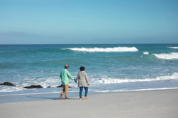 背景に青い空と海とビーチを歩いて手を取り水平線を見ているアフリカ系アメリカ人のカップルの遠くの景色 — ストック写真