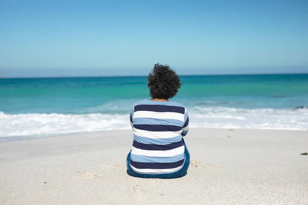后视镜 一位非洲裔美国老年妇女坐在沙滩上 背景是蓝天和大海 望着地平线 — 图库照片