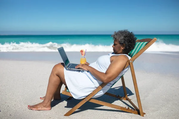 Widok Boku Starszej Afroamerykanki Plaży Słońcu Siedzącej Leżaku Korzystającej Laptopa — Zdjęcie stockowe