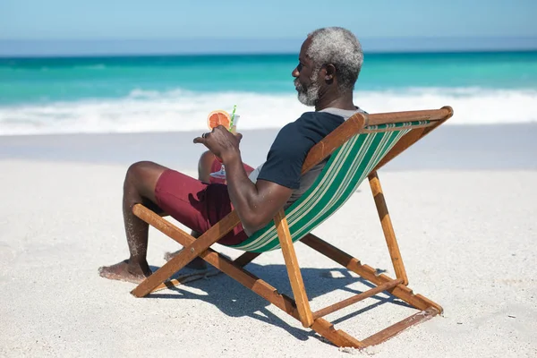 Widok Boku Starszego Afroamerykanina Plaży Słońcu Siedzącego Leżaku Trzymającego Koktajl — Zdjęcie stockowe