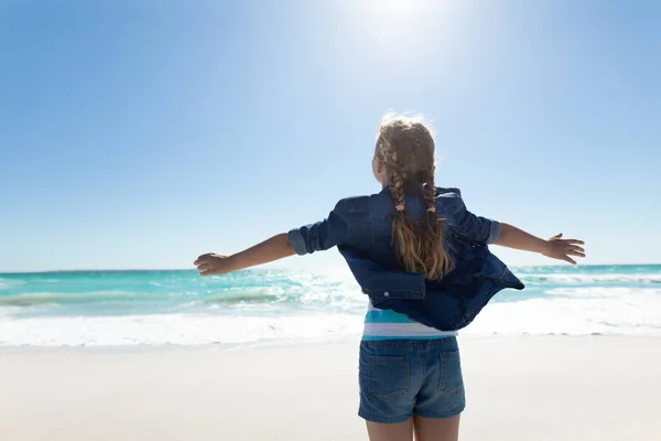 青い空と海を背景に 地平線に面した腕を伸ばして立って 日当たりの良いビーチで白人の女の子の後部ビューを閉じます — ストック写真