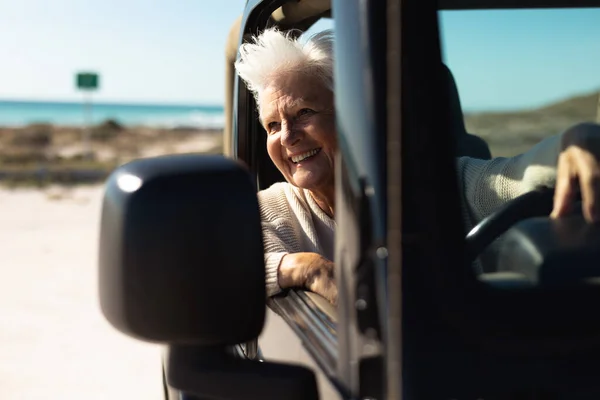 一位高个子白人妇女坐在沙滩上晒太阳 坐在驾驶座上的方向盘后面 朝窗外看去 面带微笑 — 图库照片