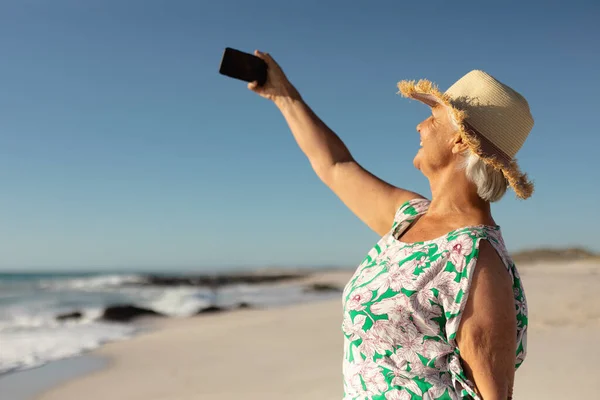 Güneş Şapkası Takmış Elinde Akıllı Bir Telefonla Arka Planda Deniz — Stok fotoğraf