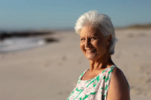 太陽の下で青い空を背景にカメラと笑顔を探して ビーチでシニア白人女性の肖像画 — ストック写真