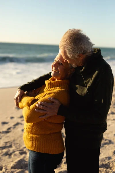 在海滩上 一对身穿毛衣 抱着孩子 面带微笑 背对着蓝天和大海的白种人老夫妻的侧观近景 — 图库照片