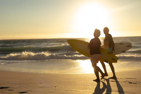 Vista Lateral Una Pareja Ancianos Caucásicos Playa Atardecer Sosteniendo Tablas —  Fotos de Stock