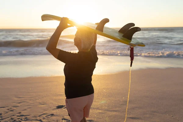 砂浜に立って海を眺めながら頭にサーフボードを抱いている白人女性の横からの眺め — ストック写真