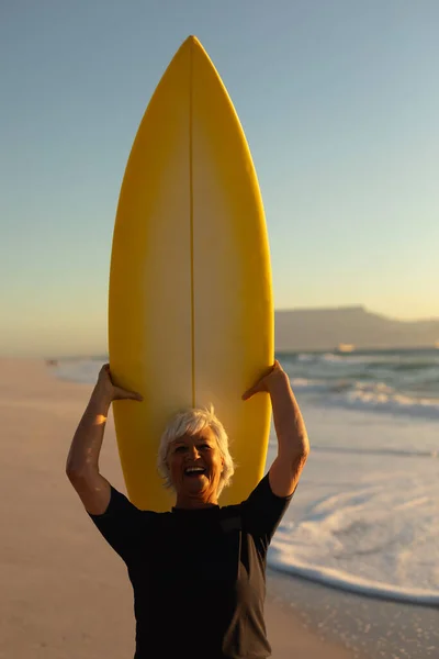夕阳西下时 一位高个子白人妇女站在沙滩上 头顶冲浪板站在沙滩上 凝视着镜头 — 图库照片