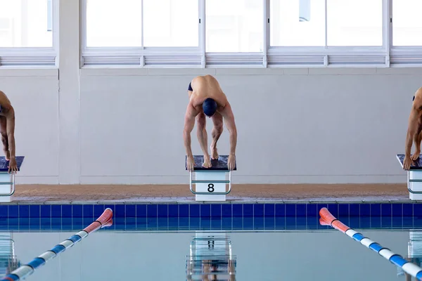 三位男子游泳运动员在游泳池前 弯腰准备从起跳台跳入水中 — 图库照片