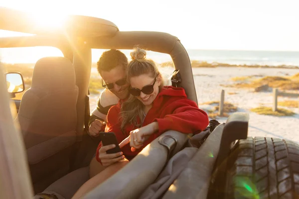一对白种人夫妇坐在敞篷轿车里 用智能手机笑着站在前看 周末海滩度假 生活方式和休闲 — 图库照片